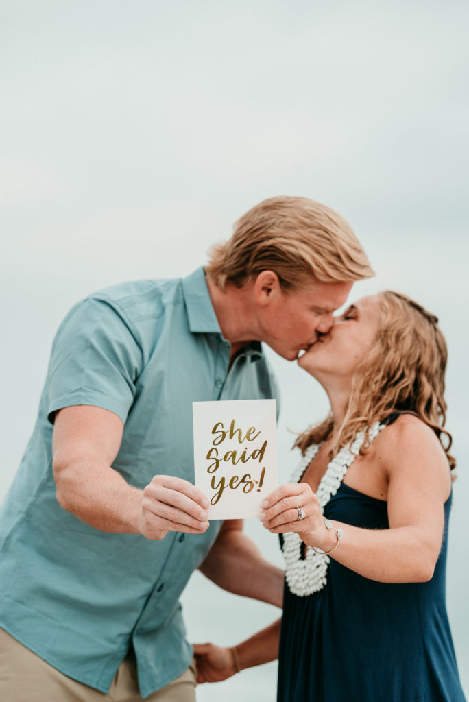 San Diego Proposal Photographer Marie Monforte captures this image of a newly engaged couple kissing while holding up a "She Said Yes" Sign. 
