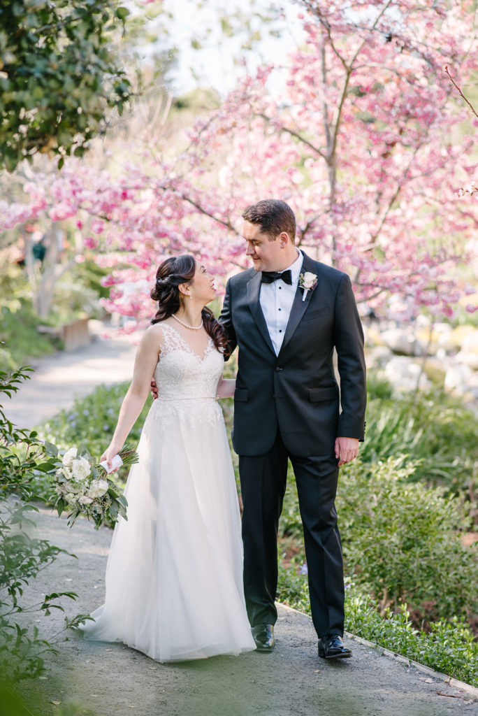 Bride and groom share a kiss among the blooming pink cheery blossoms in Balboa Park's Japanese friendship garden. 