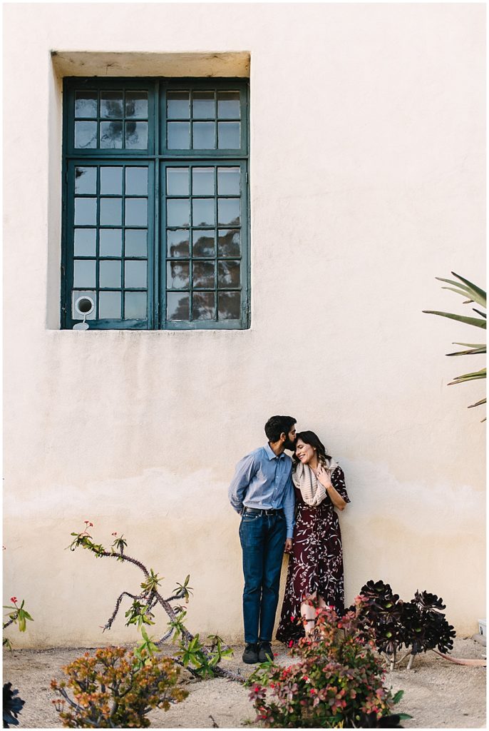 COuple shares a kiss leaning onto a wall in front of Balboa Park's Museum of Us Scientific Library. The minimalistic and start architecture of this building is in stark contrast to the intricate baroque stylings many of Balboa Park's buildings are known for.  