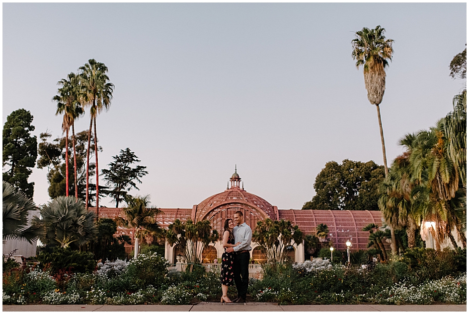 Couple poses in front of the Lily Bond and Botanical Building during their Balboa Park engagement session with photographer Marie Monforte. 