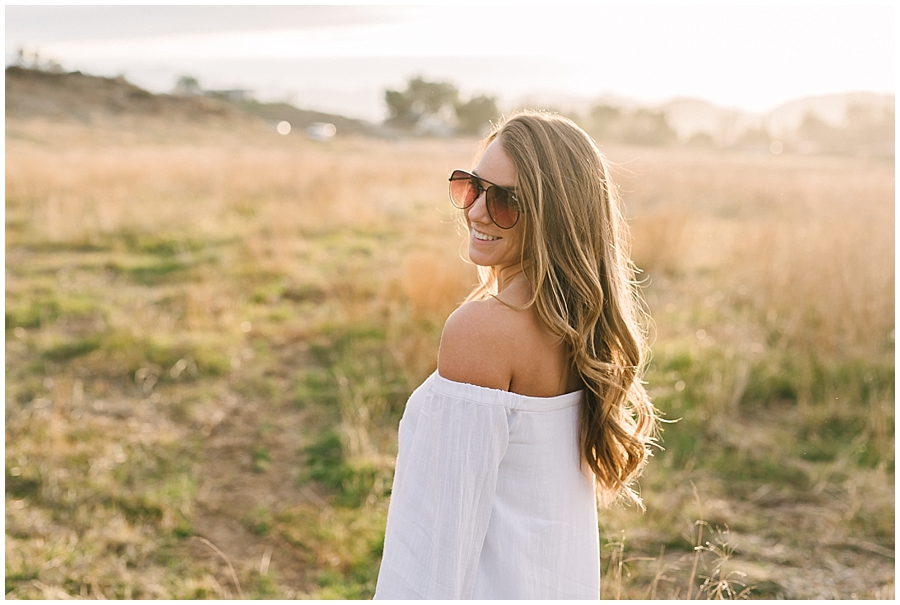 Beautiful bride-to-be in a white top and sunglasses glows with the radiance of a rising morning sun behind her. She has no idea her beau is about to propose to her n front of the rising hot air balloons in the background. 