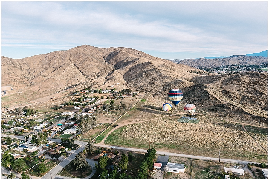 Image by San Diego Wedding Photographer Marie Monforte shows a view of Temecula hills and valleys from up in the Hot Air Balloon. Visible below are three other Hot Air Balloons that are still filling or rising. 