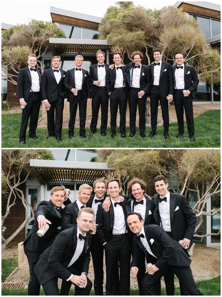 A groom stands and smiles in front of a building with his 7 groomsmen, all wearing black suits and black bow ties. 