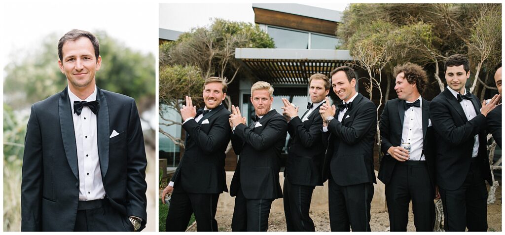 A groom stands and smiles in front of a modern building with his 7 groomsmen, all wearing black suits and black bow ties. 