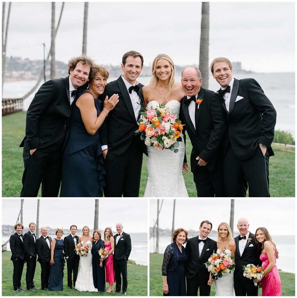 A bride and groom smile as they stand next to their friends and family on a field of grass next to the ocean. 